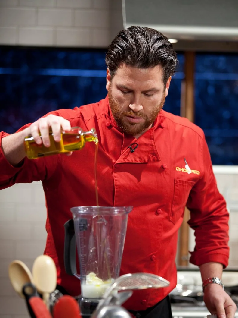 Judge and Chef Scott Conant pours oil into a blender to make a sauce, as seen on Food Network’s Chopped All Stars, Season 14.