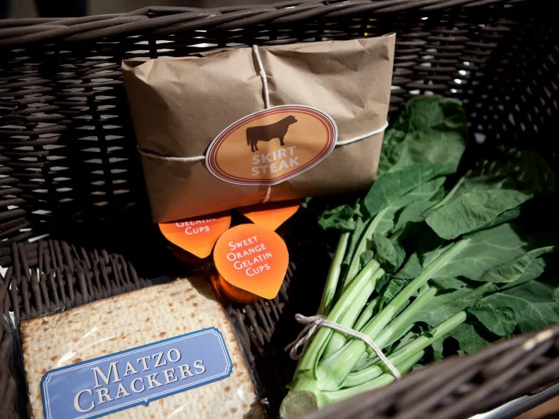 Basket ingredients for the entree round, including matzo crackers, sweet orange gelatin cups, skirt steak, and leafy greens as seen on Food Network’s Chopped All Stars, Season 14.
