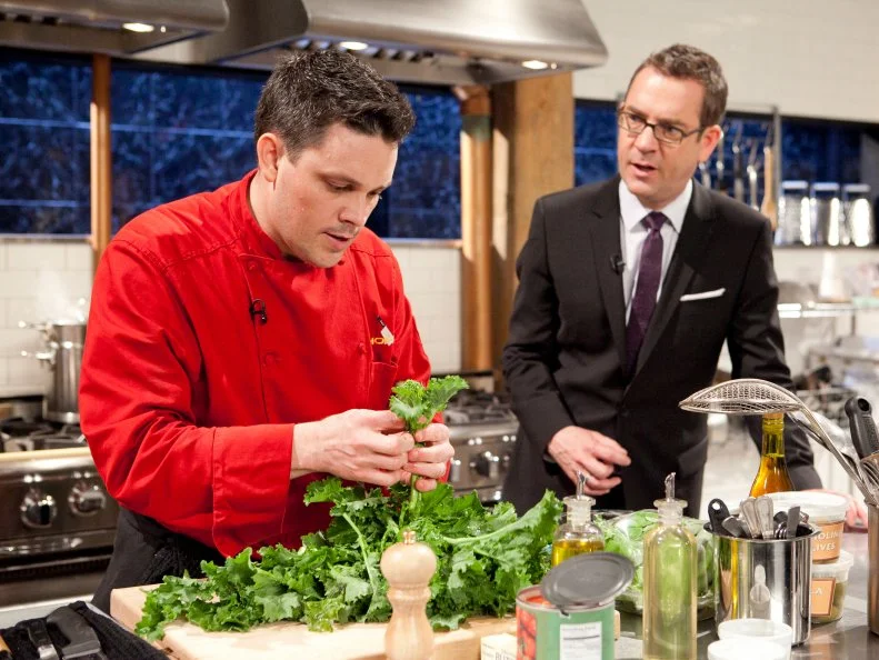 Host Ted Allen talking to All-Star Chef Gavin Kaysen while he works on his entree which must include: suckling goat, broccoli rabe, farro and cheddar filled pretzels ,as seen on Food Network's Chopped All-Stars, Season 14.