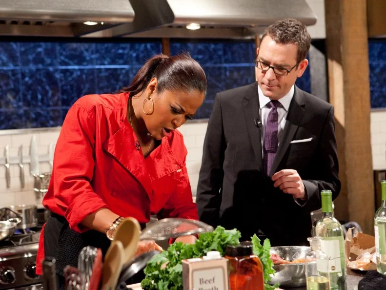 Host Ted Allen talking to All-Star Chef Laila Ali while she works on her entree which must include: suckling goat, broccoli rabe, farro and cheddar filled pretzels ,as seen on Food Network's Chopped All-Stars, Season 14.