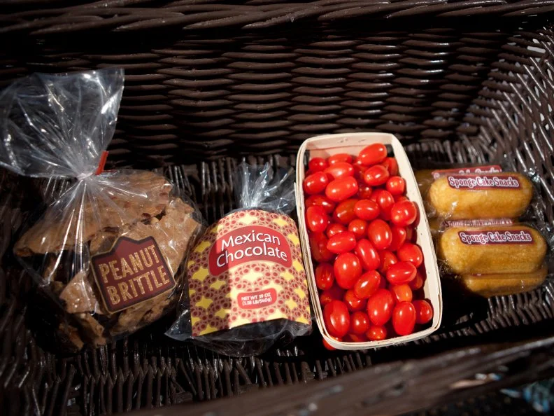 Basket ingredients for the dessert round, including peanut brittle, mexican chocolate, grape tomatoes, and sponge cake snacks, as seen on Food Network’s Chopped All Stars, Season 14.
