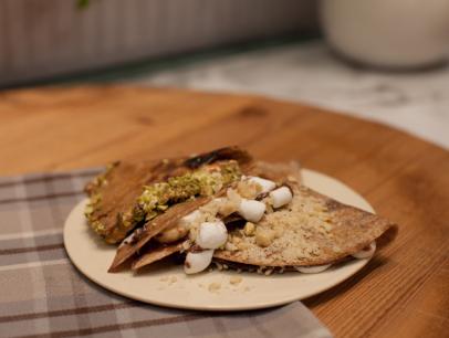 Whole wheat tortillas spread with hazelnut-chocolate spread and marshmallows. Heated on a griddle until gooey and cut into wedges. The sides are dipped in chopped hazelnuts and pistachios. Fake Crepes prepared by host Sunny Anderson as seen on Food Network's The Kitchen, Season 1.