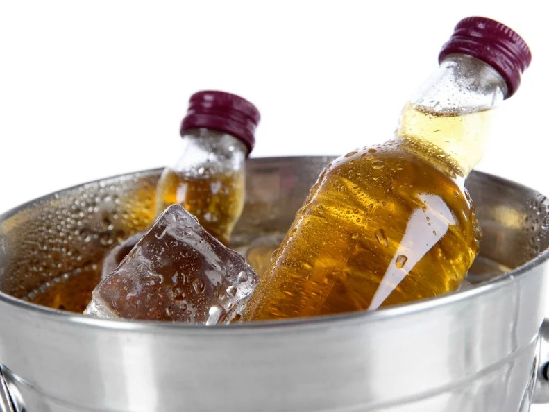 Minibar bottles in bucket with ice cubes, isolated on white
