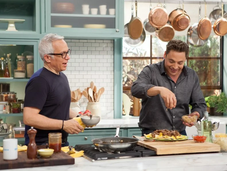 Jeff Mauro, right, tops off BBQ Nachoes with rare deli counter roast beef, as  and Geoffrey Zakarian, left, observes, as seen on Food Network's The Kitchen, Season 2.