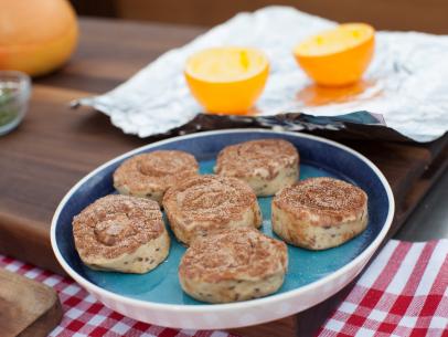 Cinnamon buns sit on a table next to orange halves, as seen on Food Network's The Kitchen, Season 2.