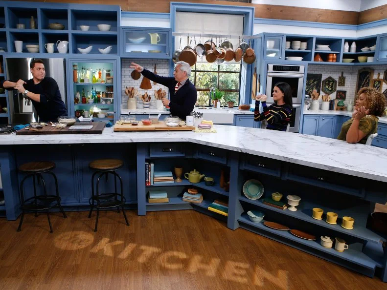 Co-host Geoffrey Zakarian, second left, demonstrates his Strawberry Cheesecake Banana Bread for fellow hosts, from left, Jeff Mauro, Katie Lee and Sunny Anderson as seen on Food Network's The Kitchen, Season 7.