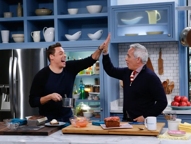 Co-host Jeff Mauro, left, demonstrates his Bananas Foster Banana Bread for fellow host Geoffrey Zakarian as seen on Food Network's The Kitchen, Season 7.
