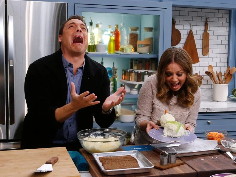 Hosts Jeff Mauro and Marcela Valladolid react as Valladolid's Snowman Cheeseball collapses as seen on Food Network's The Kitchen, Season 8.