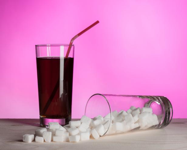 Glass of cola and another full of sugar on the side.  Representing how much sugar can be in cola drinks.