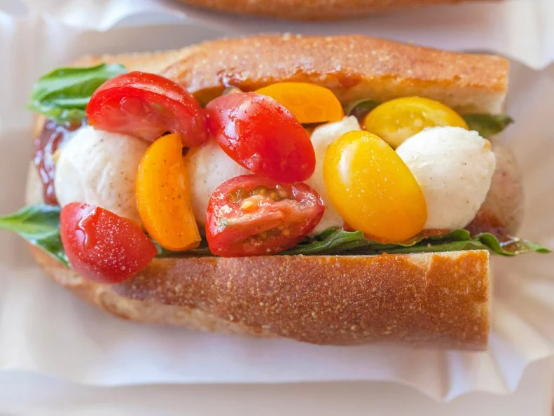 Jackie Alpers for the Food Network. Caprese  hot dog with balsamic ketchup, heirloom tomatoes, basil, mossarella, salt and pepper on a baguette.