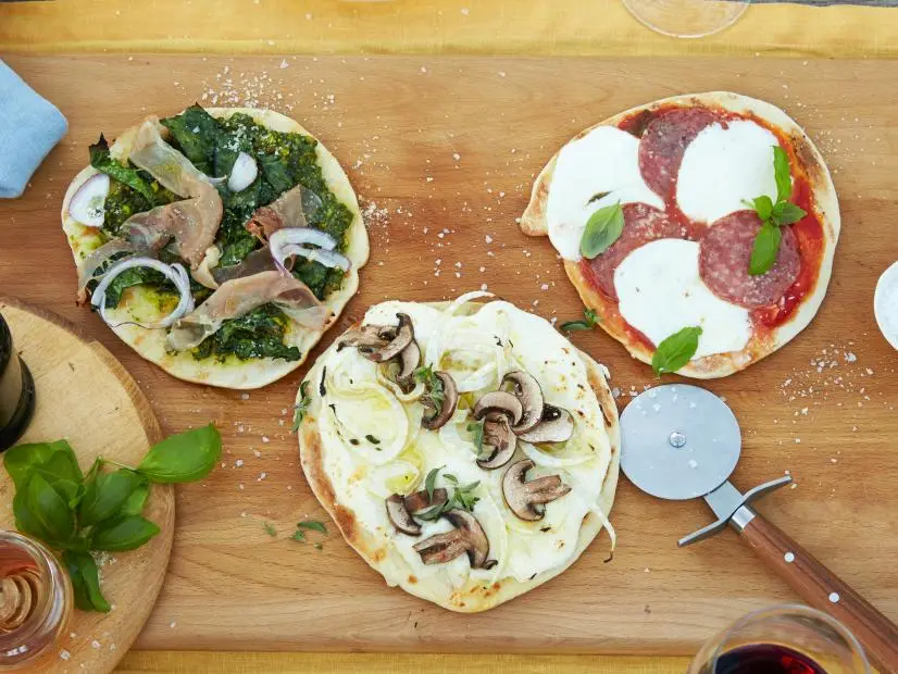 GRILLED PIZZA FOR A CROWD, Food Network Kitchen, Food Network, Bread Flour, Kosher
Salt, Olive Oil, Sugar, Active Dry Yeast, Cornmeal, Mozzarella, Fontina, Asiago, Prosciutto,
Salami, Ham, Tuscan Kale, Bell Peppers, Mushrooms, Red Onions, Figs, Corn, Olives,
Pistachios, Fennel, Summer Squash or Zucchini, Radicchio, Balsamic Vinegar, Calabrese
Chili Sauce, Honey, Parmesan, Sea Salt, Fennel Seeds, Baby Greens, Basil, Lemon
Wedges, Tomato Sauce, Garlic, Arugula, Parsley, Capers, Ricotta