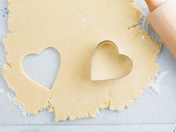Heart shaped cookie cut out of cookie dough with cutter and rolling pin