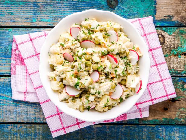 potato salad with fresh radishes in a white bowl on a rustic wooden table
