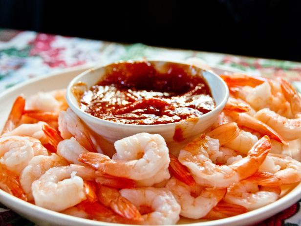 A bowl of tomato-based dip sits amidst a plate of cooked shrimp.