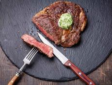 Medium rare grilled Beef steak with herb butter on fork on dark background