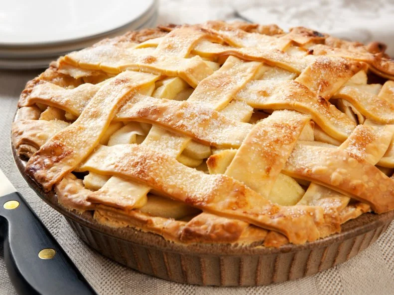 Home-baked lattice apple pie, in a brown ceramic pie plate, ready to serve.