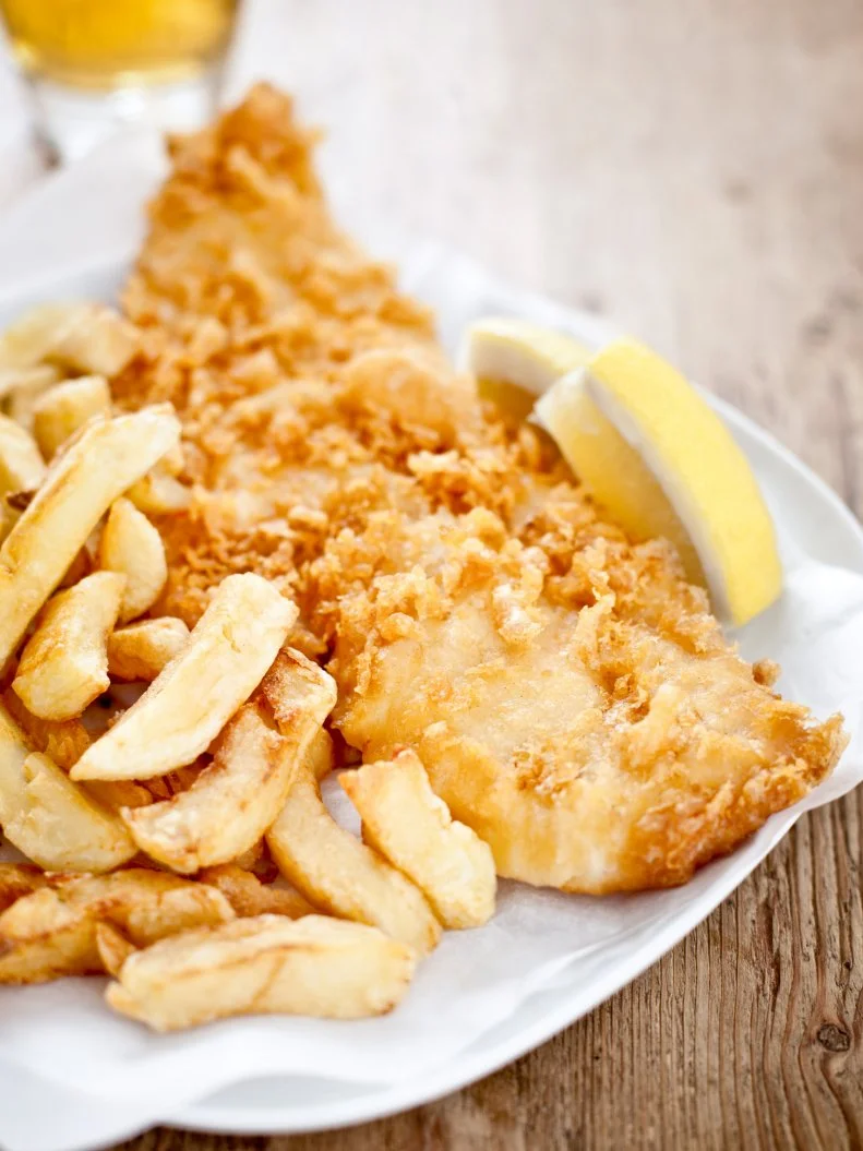 Plate of traditional English fish and chips sitting on a wooden table with a slice of lemon.
