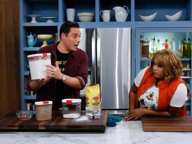 Host Jeff Mauro demonstrates a pantry tip for fellow host Sunny Anderson during a segment about organizing a holiday cookie pantry, as seen on Food Network's The Kitchen, Season 11.