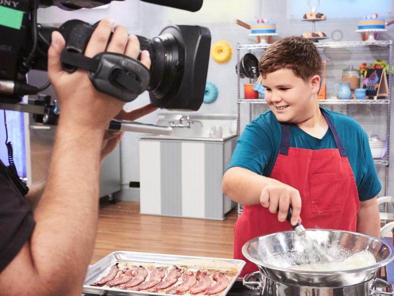 Contestant Aidan Berry preparing his Main Heat dish, Maple Cupcake with Maple, Chocolate Banana Frosting and Bacon, with the Chocolate Covered Banana Carnival Treat, as seen on Food Network's Kids Baking Championship, Season 3.