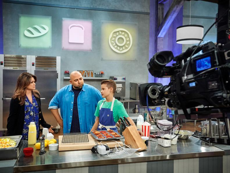 Hosts Valerie Bertinelli and Duff Goldman watches Contestant Cole Frederickson preparing his Main Heat dish, Yellow Cupcake with Deep Fried Chocolate Sandwich Cookies and Root Beer Buttercream, with the Cotton Candy Carnival Treat, as seen on Food Network's Kids Baking Championship, Season 3.