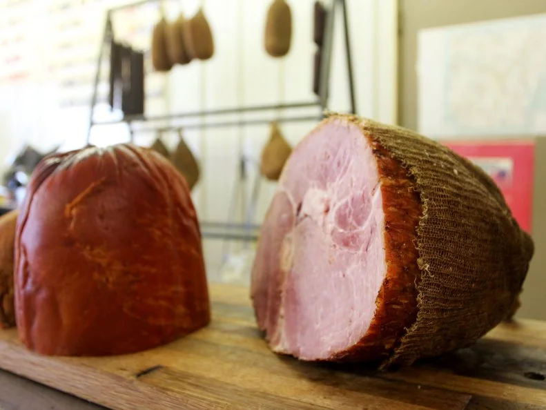 Smoked ham with hams, turkey and sausages in background at Coursey's Smoked Meats in St. Joe, Arkansas, as included in Arkansas's Most Iconic Eats for FoodNetwork.com.