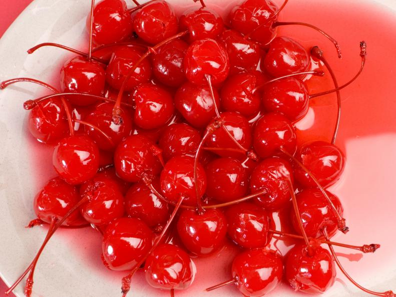Festive background of red cocktail maraschino cherries with stems - close up on a white stone plate