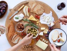 Hands reaching for food on a well spread cheese platter, party snack appetiser with wine