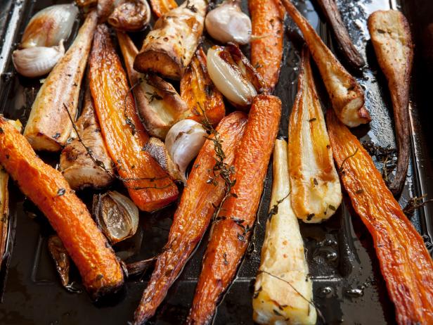 Carrots and parsnips roasting in a pan, with thyme, shallots, and garlic.