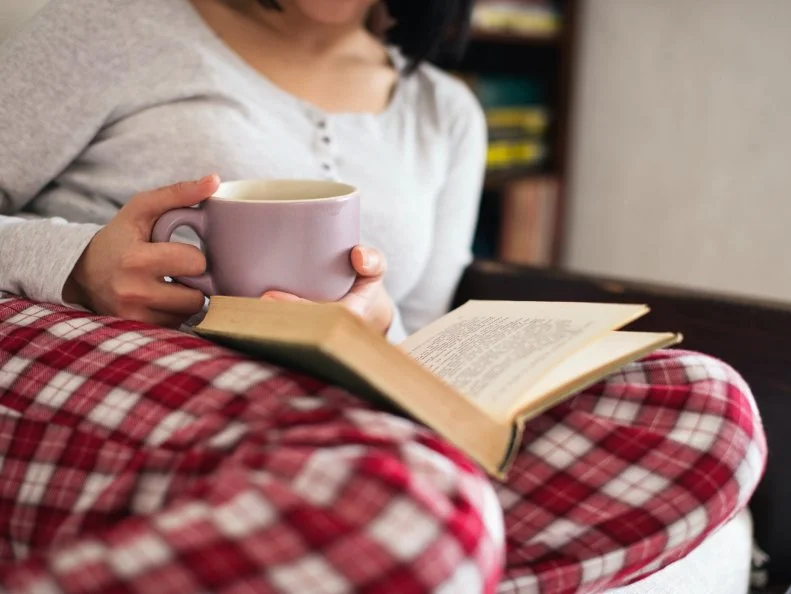 Women in her living room reading book and drinking tea