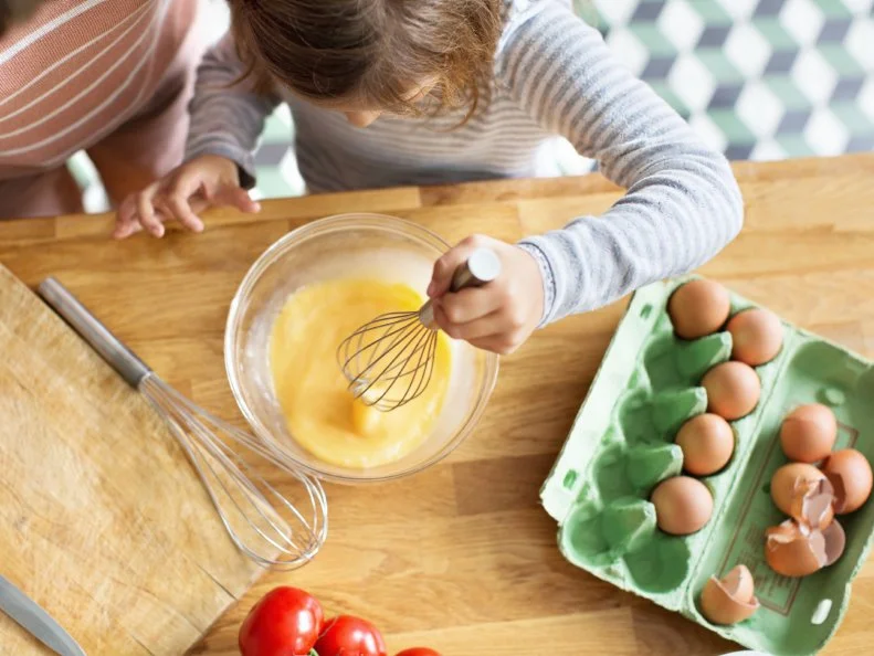 Top view of young girl whipping eggs in a bowl with a wire whisk in kitchen