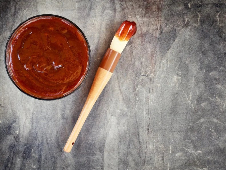 Barbecue sauce with basting brush over stone table with room for copy space.