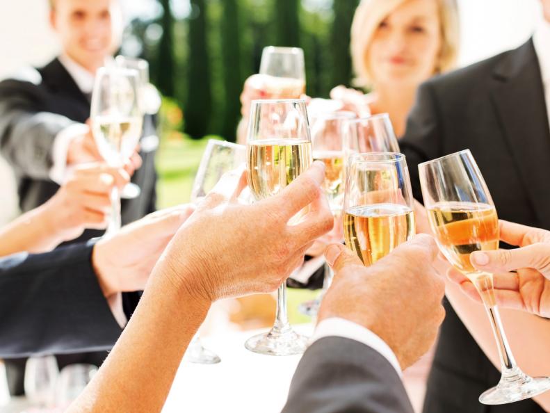 Close-up of wedding guests and couple toasting champagne flutes at reception. Horizontal shot.