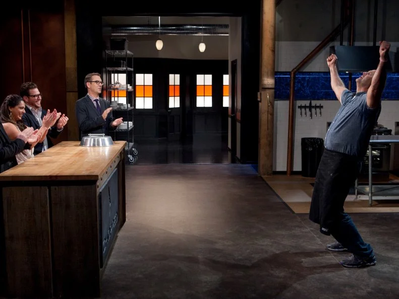Keith Young standing before Chopped host Ted Allen and judges Chris Santos, Maneet Chauhan and Scott Conant moments after finding out that he is a Chopped Champion, as seen on Food Network's Chopped, Season 19.