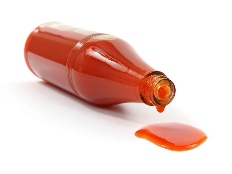A bottle of hot sauce on it's side spilling onto a white background.