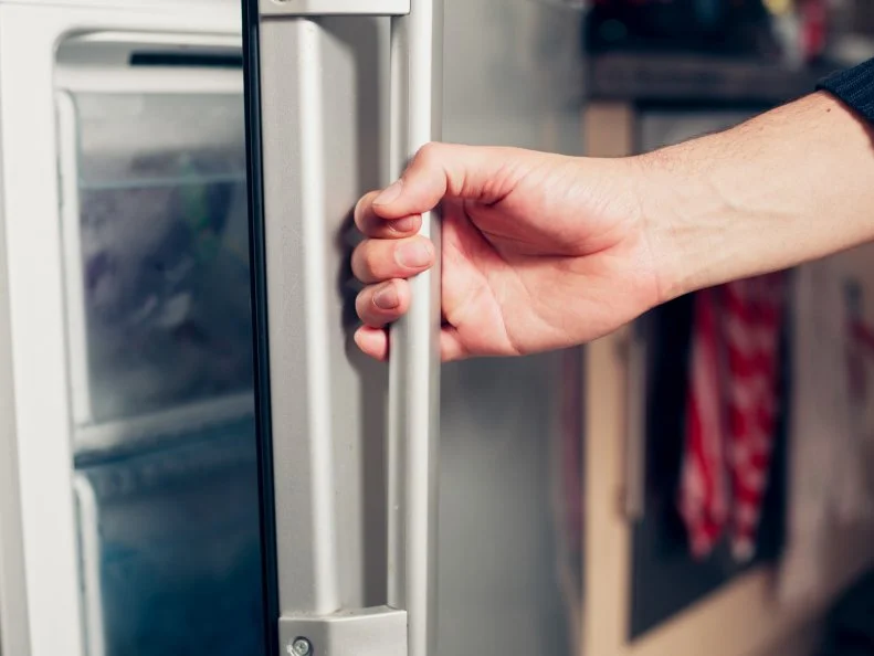 The hand of a young man is opening a freezer door