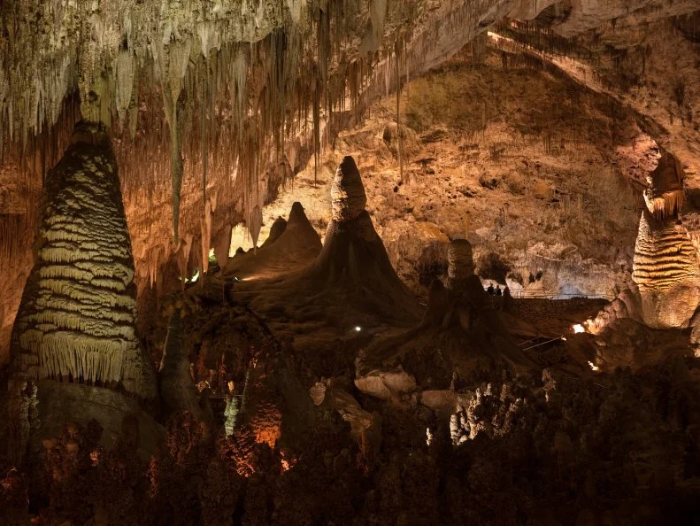 Tiny, silhouetted visitors sit in the middle of the Big Room Route dwarfed by huge stalagmites and stalactites in Carlsbad Caverns National Park located in the Guadalupe Mountains, New Mexico.