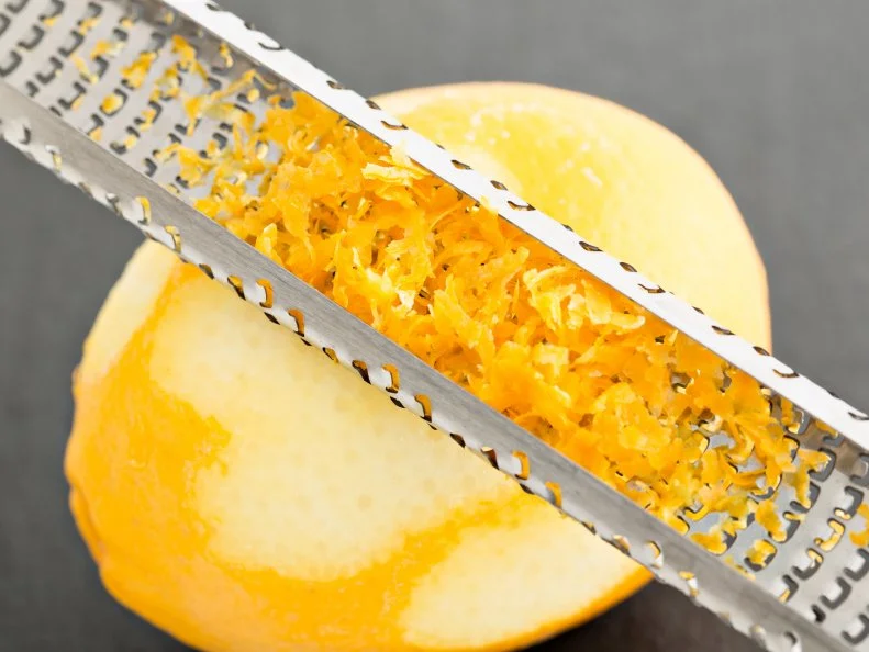 A high angle close up shot of a chef zesting a lemon with a microplane grater.