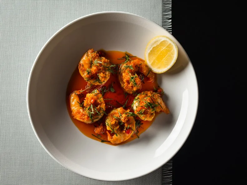 Wild gulf shrimp over garlic and chili oil and garnished with thinly chopped herbs and a slice of lemon in a white bowl on a fringed white mat over a black surface prepared by Executive Chef Jean-Georges Vongerichten at the Edition Hotel, Miami Beach FL