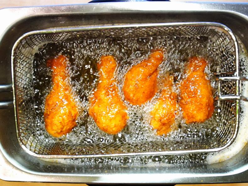Closeup top view of several pieces of chicken being fried in a stainless steel deep fryer. Sparkling and greasy chicken thighs.