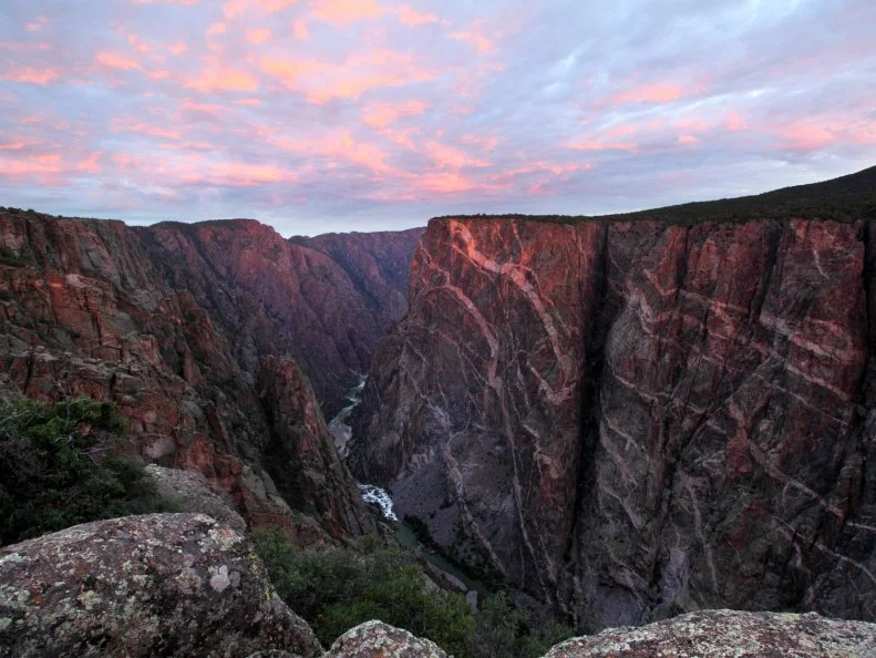 Sun rises over Black Canyon of the Gunnison, Colorado. This cliff is the Painted Wall, the tallest vertical cliff in Colorado, at 2,722 feet. Sunlight barely peeks through the clouds to brighten the top of the cliff with a touch of sunlight.