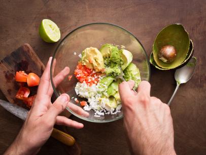 Mashing vegetables to make guacamole on wooden table overlook