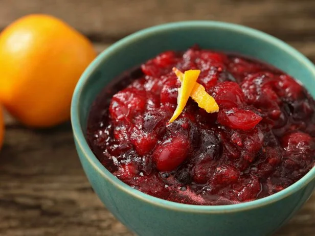 A high angle close up horizontal photograph of a turquoise bowl full of homemade cranberry sauce made with freshly squeezed tangerine juice and a couple of fresh tangerines.