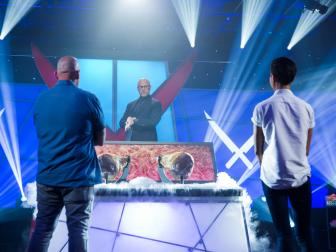 Contestants Matt Jennings (L) and Kristin Kish with Host Alton Brown as he introduces the secret ingredient for the Chairman's Challenge, Prosciutto, as seen on Iron Chef Showdown, Season 1.