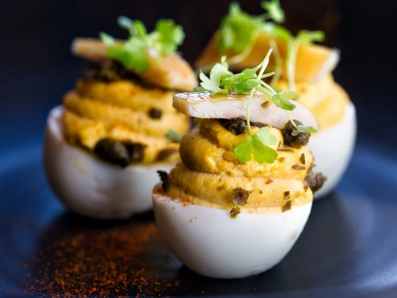 To be popular at a Kentucky potluck, bring deviled eggs, and watch your platter empty before all others. While each Kentucky cook makes deviled eggs to suit family preferences, ranging from purely savory to sweet-tart, Kentuckians are broad-minded and enjoy the full flavor spectrum. Although restaurants rarely feature deviled eggs, Dudley’s Restaurant, founded in Lexington in 1981, offers acclaimed daily deviled egg appetizers, with optional Kentucky smoked trout and fried caper toppings. Some Kentuckians resist the “devil” in deviled eggs, perhaps not trusting the late 18th-century British, who began using the term to describe certain intensely flavored, stimulating foods. While Kentuckians claim deviled (or “dressed” or “stuffed”) eggs as their own, versions of this favorite bite appear on tables around the world, and have since the days of the ancient Romans.