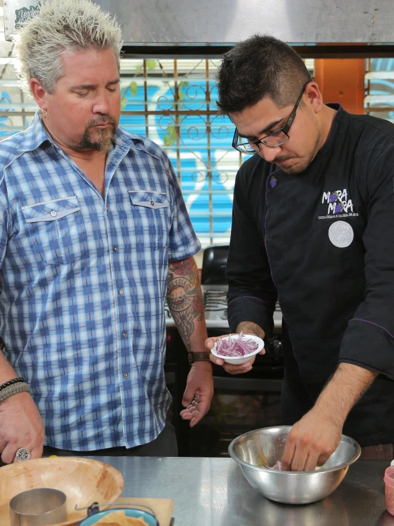 Host Guy Fieri observing Chef and Owner Christian Rodriguez in action at Mora Mora in Quinta La Ceiba, Cancun, Mexico as seen on Food Network's Diners, Drive-Ins and Dives episode 2606.