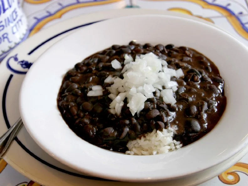 Adapted from their grandmother's recipe, the owners of Columbia Restaurant serve up an authentic bowl of Cuban black bean soup Frijoles Negros that has become well-known amongst Floridians looking for an authentic Cuban meal. The rustic, completely vegetarian soup is made with beans, green peppers, onions and a variety of seasonings, served on a bed of rice and topped with raw Spanish onions.