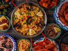 Typical spanish tapas concept. Concept include slices jamon, bowls with olives,  anchovies, spicy potatoes, mashed chickpeas, shrimp, calamari, manchego with quince marmalade, pans with tortilla, paella, mussels  on a wooden table.