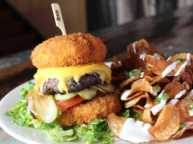 Executive Chef Keith Williamson is a big fan of fiery mac and cheese. His menu at Datz is filled with dairy-coated pasta options: the somewhat straightforward jalapeno-bacon mac and cheese, spicy fried mac and cheese bites, and more. That cheesy chile-pork combination, however, is also used as a substitute for another carb; Williamson makes bacon-jalapeno mac and cheese "buns." For his Cheesy Todd, Williamson coats circular pasta patties in panko and fries them until browned. The bottom "bun" is placed on a plate, layered with a grilled hamburger patty, thinly sliced pickles, tomato, onion and lettuce, then topped with the crisp round and secured with a skewer. If ever there were a knife and fork burger, this would be it.