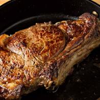 A high angle extreme close up horizontal photograph  of a sizzling bone in rib eye steak in a black cast iron pan.