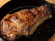 A high angle extreme close up horizontal photograph  of a sizzling bone in rib eye steak in a black cast iron pan.